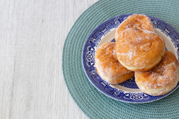 Jam doughnuts on a blue and white plate and green table mat on a grey wood background