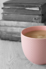 Cup of tea in a pink cup on a stack of old antique books with selective colour on a grey wood background