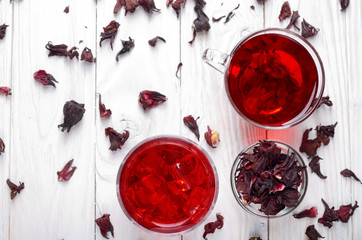 Top view at two tea cups with ice and dry hibiscus petals on white wooden table background