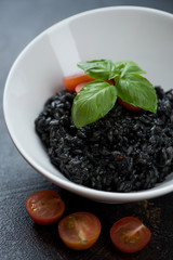 Risotto with squid-ink served in a white bowl, selective focus, closeup, vertical shot
