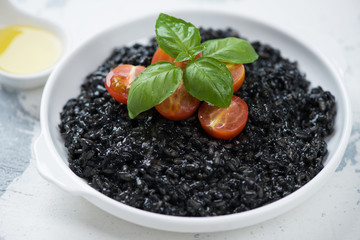 Risotto with squid-ink, cherry tomatoes and fresh green basil in a white plate, close-up