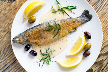 baked flour coated trout with gravy on white wine, served with fried rosemary, lemon slices, and olives