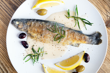 piquant fish with gravy on white wine, served with fried rosemary, lemon slices, and olives