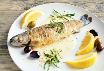 baked trout served with gravy, fried rosemary, lemon slices, and olives 