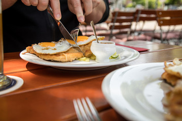 Mann isst Schweine Fleisch Schnitzel Wiener Art mit Spiegelei als Hamburger dazu Gurken Kartoffelsalat und Bayrischen süßen Senf im Biergarten Restaurant