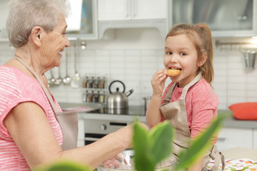 Cute girl and her grandmother cooking in kitchen