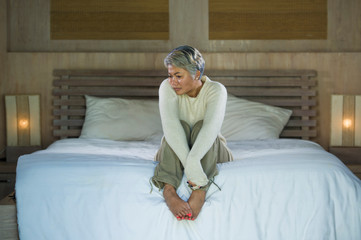 dramatic lifestyle home portrait of attractive sad and depressed middle aged woman with grey hair on bed feeling upset suffering depression and anxiety