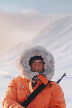 young female hunter wearing an orange jacket with fur and behind there is winter landscape in sunset 