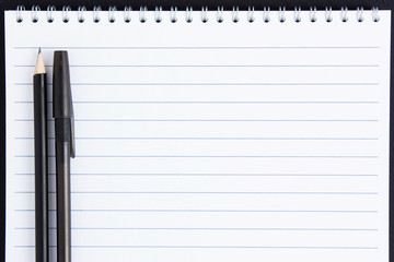 Black pen and pencil lie on a white notebook.