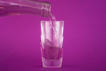 Purple carbonated liquid (water) is poured into a glass or shot from a bottle on a violet background