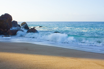 breaking wave on shoreline with backwash, backspray, with sandy beach, against cliff with rocks
