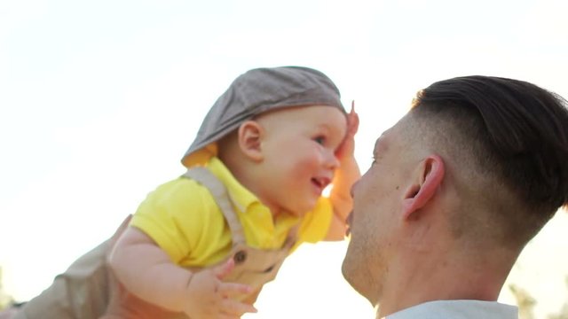 Happy young father throws up the kid upwards on sunset sky background and sunlight. Father's day, family concept