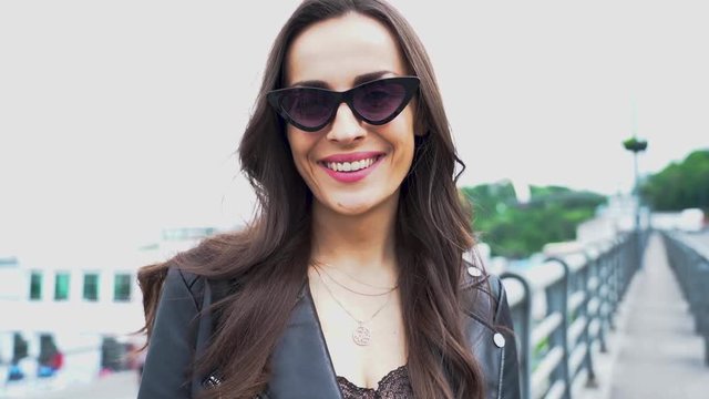 Slow motion shot of smile brunette woman in sunglasses posing on the street outdoors and looks on the camera