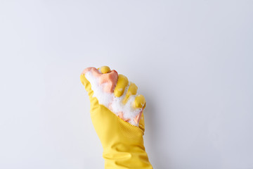 Hand in glove with a sponge for washing. Hand in a protective glove with a washing sponge on light background. Time for clean up.