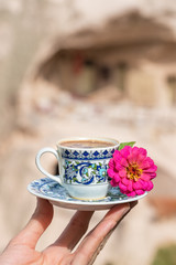 Womans hand holding a cup of traditional turkish coffee with famous Uchisar Castle at background in...