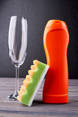 Accessories for dishwashing and house cleaning. Bottle of detergent, glass and sponge on dark background. Dishwashing concept.