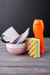 Plates, cup, detergent and sponge. Stack of clean plates, glass cup and cleaning product on wooden table. Household chores concept.