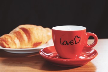 Red mug of coffee and croissant on wooden table, morning, love or healthy concept