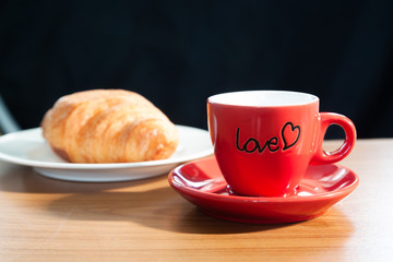 Red mug of coffee and croissant on wooden table, morning, love or Valentine's day