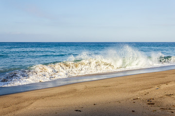 splashing breaking wave on sandy shore with backwash and horizon