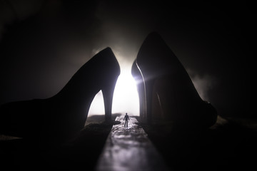 Artwork decoration. Silhouette of a man standing in the middle of the road on a misty night with giant high heel women shoes. Women power or women domination concept.