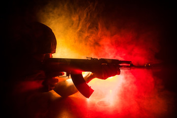 Silhouette of man with assault rifle ready to attack on dark toned foggy background or dangerous...