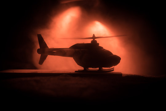 Silhouette of military helicopter ready to fly from conflict zone. Decorated night footage with helicopter starting in desert with foggy toned backlit. Selective focus.