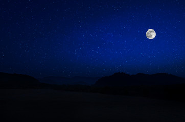 Mountain Road through the forest on a full moon night. Scenic night landscape of country road at night with large moon. Long shutter photo