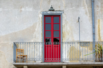 Fototapeta na wymiar porta finestra rossa su balcone con sedia antica casa italia
