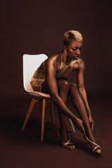 fashionable african american woman with short hair sitting on chair on brown