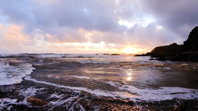 Slow motion scenic shot of beautiful california beach sunset as wave surges up coastal river, mesmerizing confluence of motion