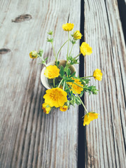 Yellow wild summer flowers in blue ceramic vase, on wooden veranda background. Still life in rustic style. Close up view. Spring in garden, countryside lifestyle concept. Copy space