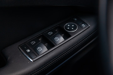 Obraz premium The control buttons for opening and closing windows of doors and electric controls and settings of mirrors on the door in black with leather upholstery in a luxury modern car.
