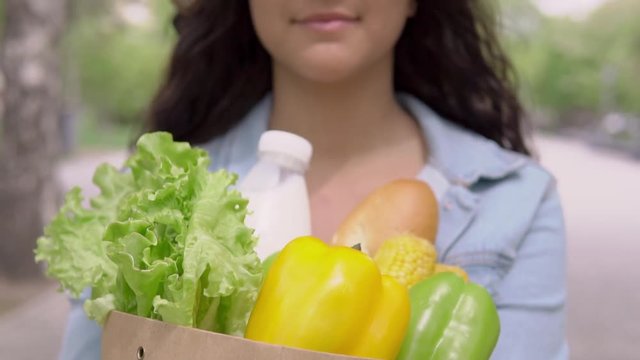 A young beautiful woman in a denim jacket and hat in a good mood carries a bag of groceries and smiles. Slow motion. Close-up