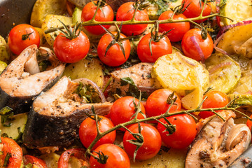 Home-made roast with vegetables and fish pieces on a baking sheet - trout, zucchini, cherry tomatoes on a branch, potatoes, onions, top view