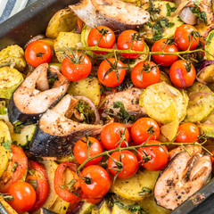 Home-made roast with vegetables and fish pieces on a baking sheet - trout, zucchini, cherry tomatoes on a branch, potatoes, onions, top view
