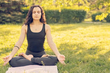 Young Caucasian woman doing yoga in the Park. Sitting in Lotus position