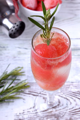 Sparkling cocktail with watermelon balls and rosemary in a champagne glass on white table