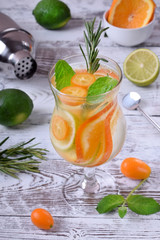 Sparkling beverage with slices of lime, kumquat and orange topped with mint against the white wooden background