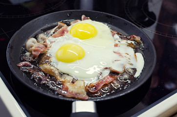 scrambled eggs cooking in a frying pan, cooking on a ceramic stove, scrambled eggs with bacon