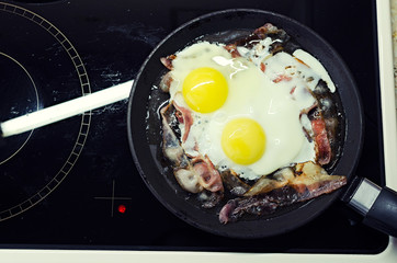 scrambled eggs cooking in a frying pan, cooking on a ceramic stove, scrambled eggs with bacon, top view