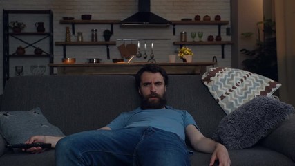 Boring, tired man sitting on the sofa and watching TV. Trying to choose interesting TV channel. - Powered by Adobe
