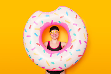 Photo of girl in swimming goggles, swimsuit with donut life buoy on empty orange background - obrazy, fototapety, plakaty