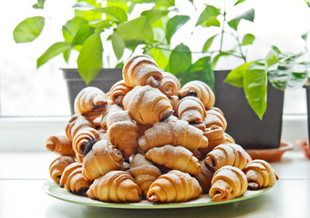Buns in a plate full of freshly baked bagels sprinkled with powdered sugar on the kitchen table. cooking baking. croissants baking preparation stage. breakfast closeup copy space