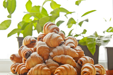 Buns in a plate full of freshly baked bagels sprinkled with powdered sugar on the kitchen table. cooking baking. croissants baking preparation stage. breakfast closeup copy space