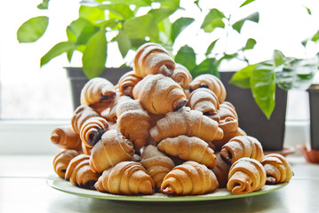 Buns in a plate full of freshly baked bagels sprinkled with powdered sugar on the kitchen table. cooking baking. croissants baking preparation stage. breakfast closeup copy space