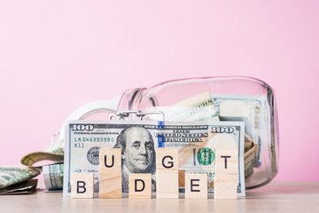 Saving money and planning budget concept. Dollar bills in glass saving bank and word budget on a pink background