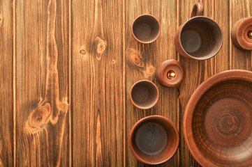 Fototapeta premium Top view set of empty rustic tableware ,clay cups and plates on a wooden brown background.Kitchen background with copy space.