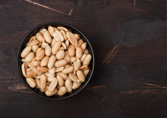 Salted and roasted peanuts classic snack in black bowl on wooden background.