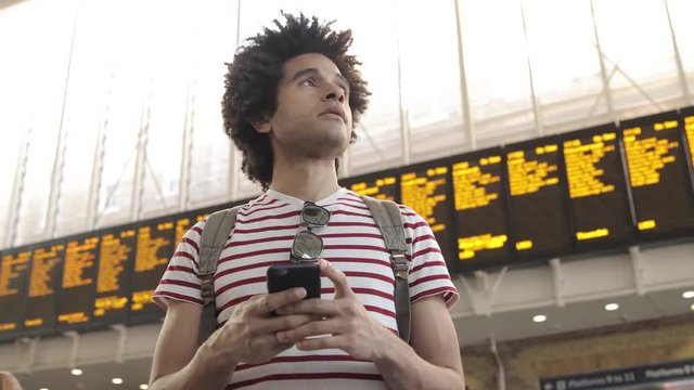 Man at train station checking timetables on mobile phone